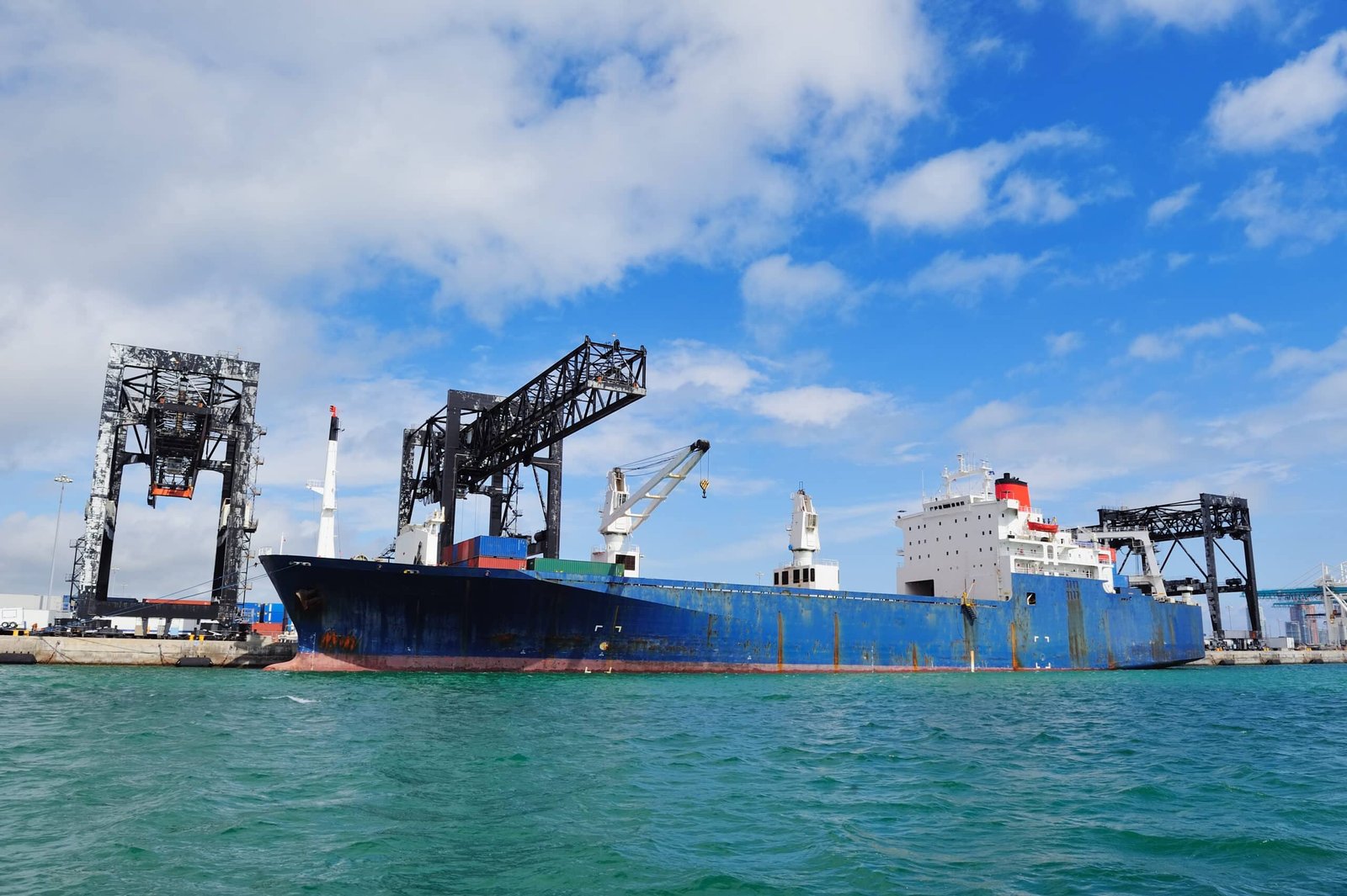 A large cargo ship docked at an industrial port with cranes loading and unloading goods. The image represents international trade, global supply chain solutions, and logistics management for diverse industries.