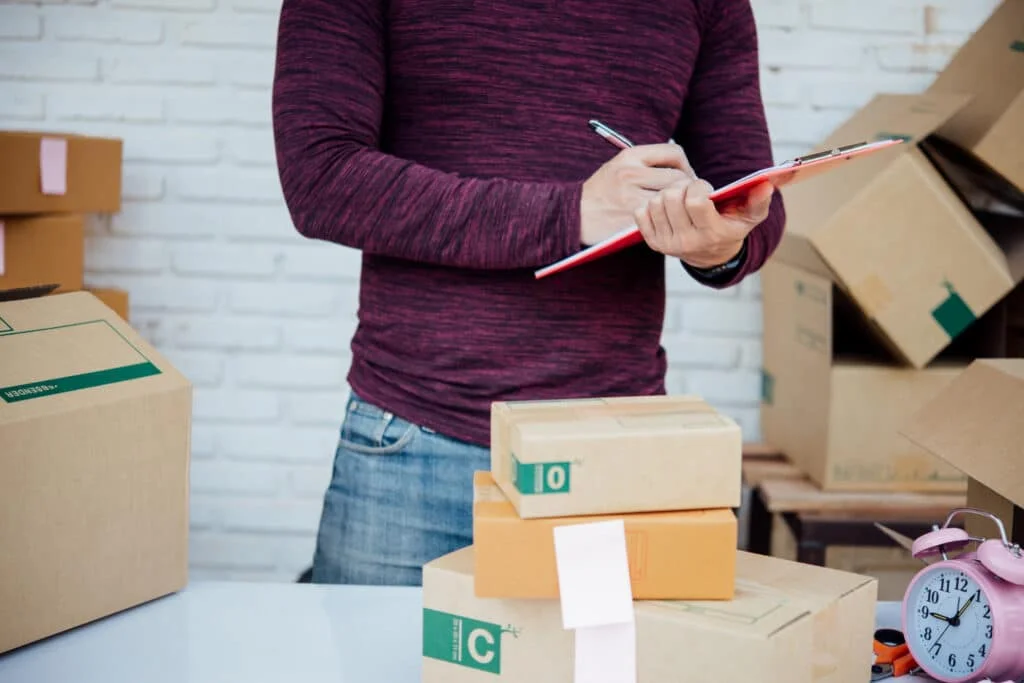 A person holding a clipboard and inspecting stacked packages, symbolizing the importance of goods classification, trade compliance, and accurate tariff determination in global commerce.