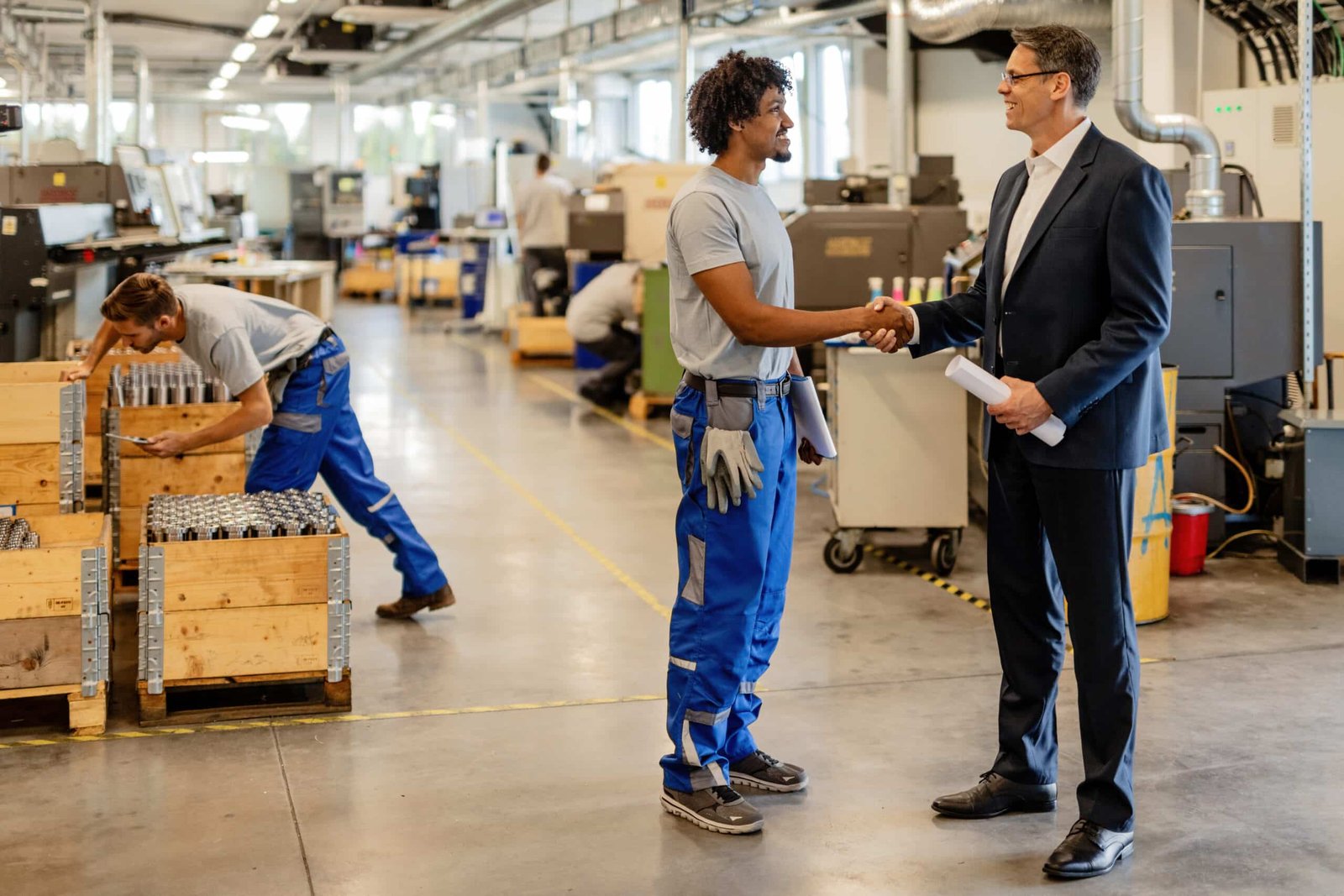Industrial worker shaking hands with manager while greeting inside manufacturing facility.
