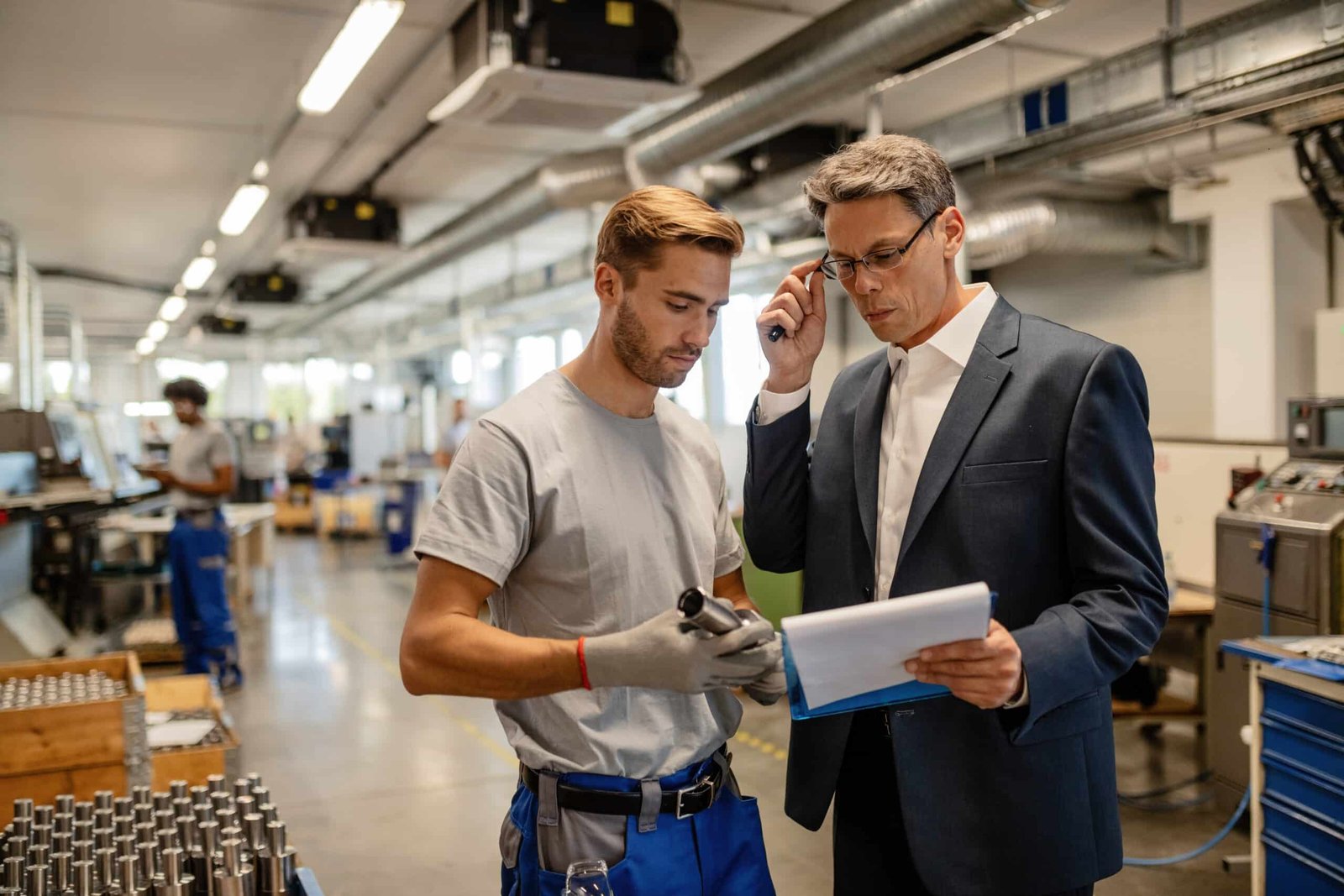 Mid-adult engineer and young worker cooperating while analyzing a factory report.